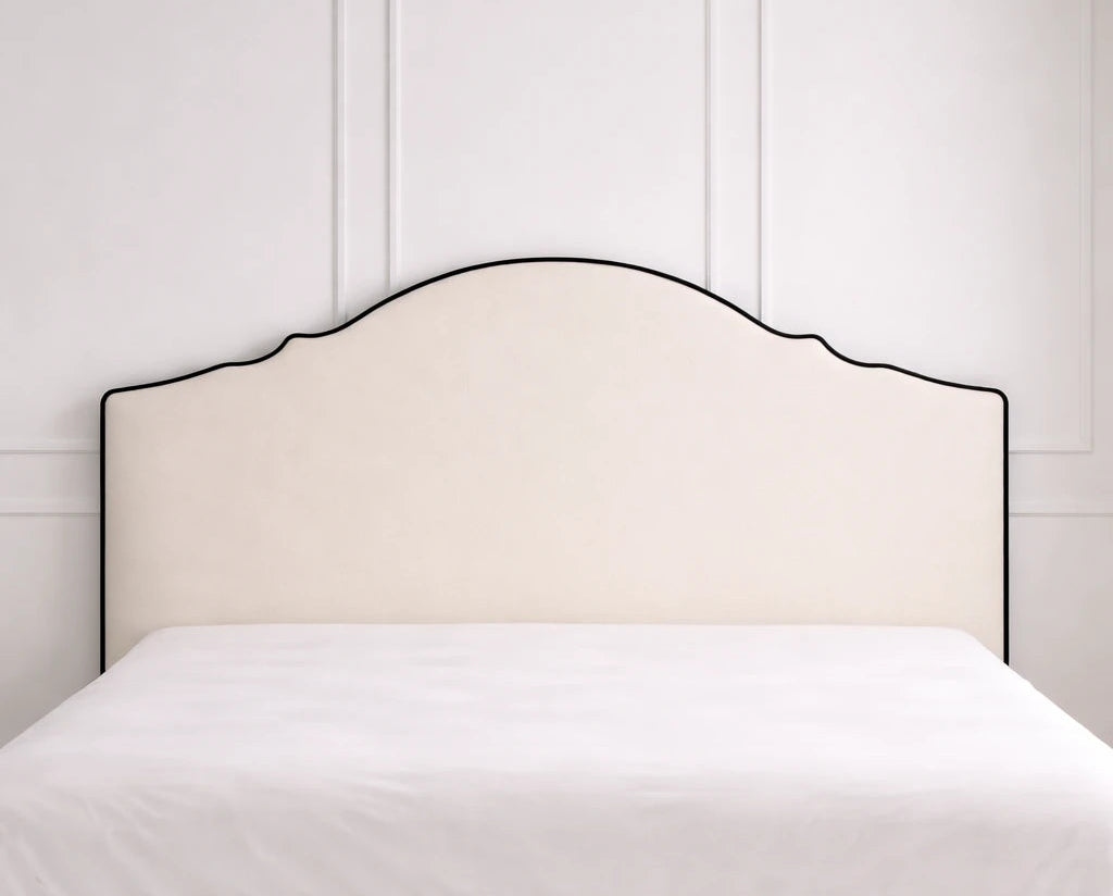 Cabecero tapizado liso crema con contorno arqueado y ribete negro contrastante, forma de arco suave estilo vintage moderno.