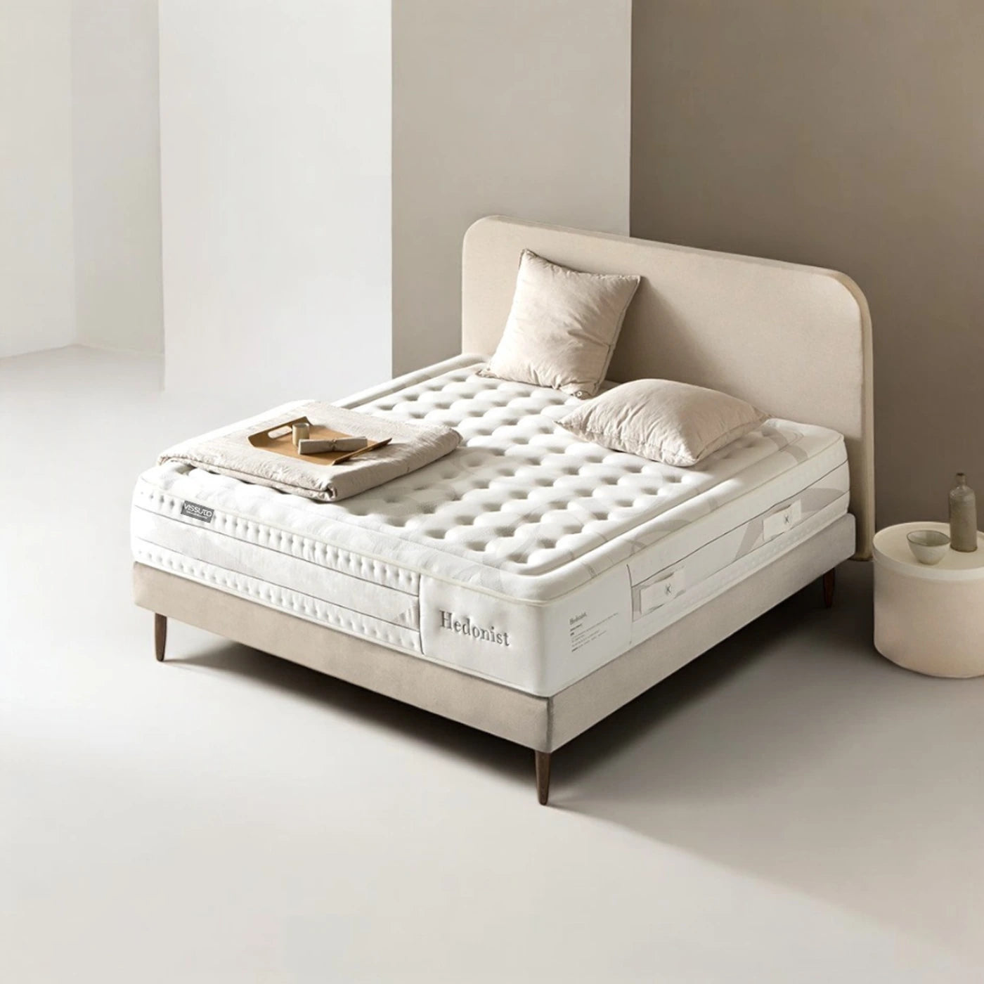 Colchón Vissuto Hedonist sobre estructura de cama con cabecero beige y cojines en dormitorio minimalista