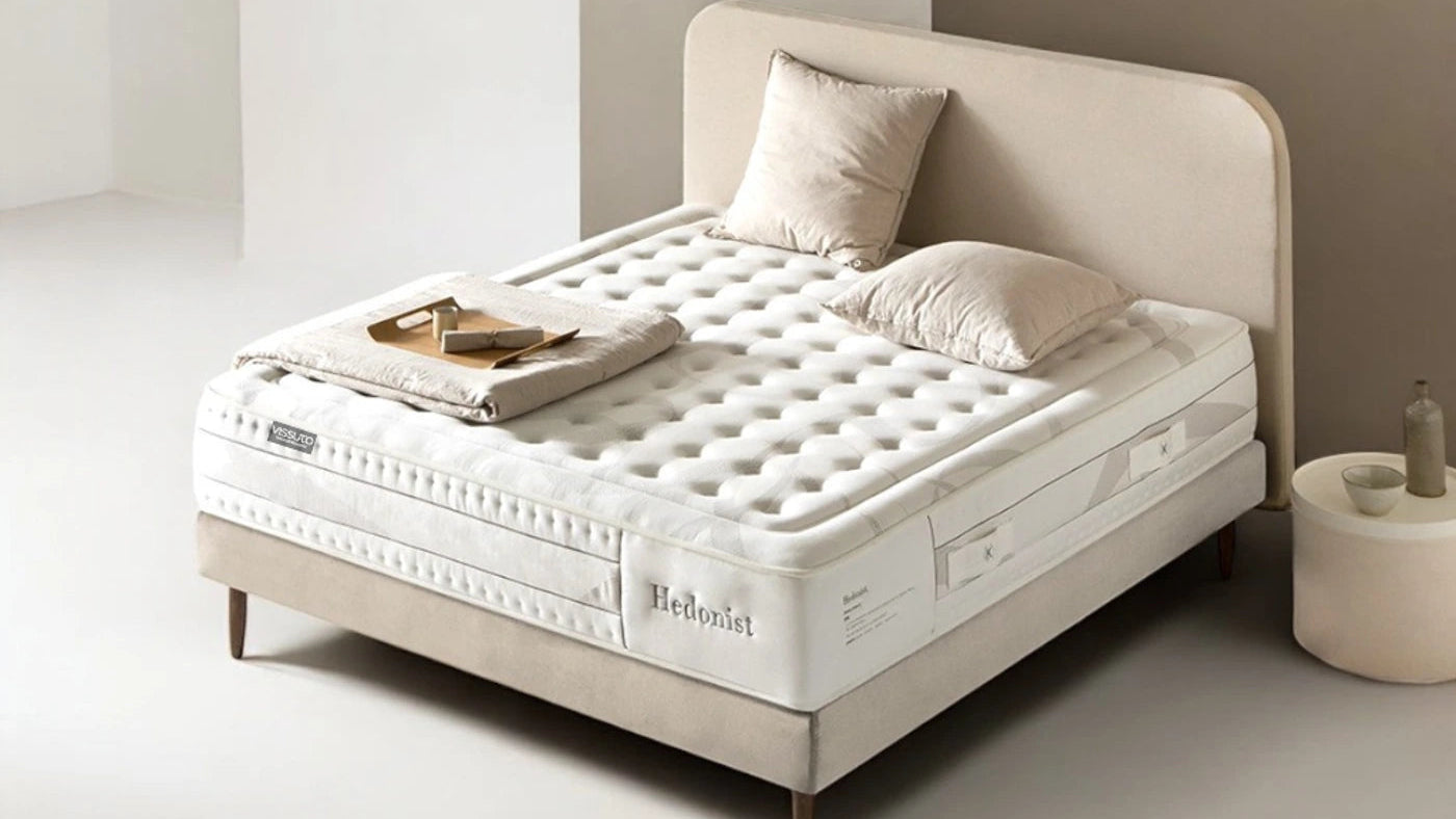Colchón Vissuto Hedonist sobre estructura de cama con cabecero beige y cojines en dormitorio minimalista